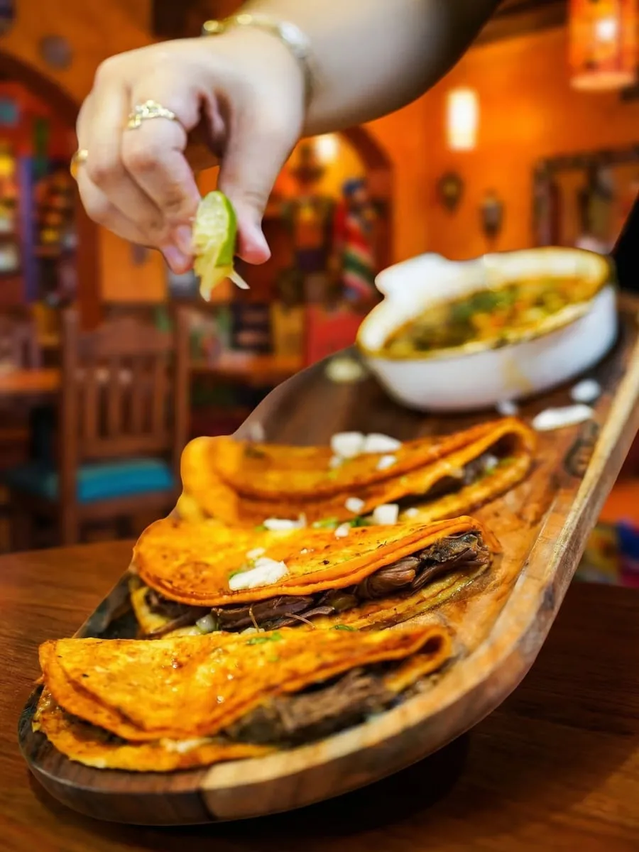 Hand squeezing fresh lime over golden birria tacos at Ixtapa Mexican Restaurant, Lunenburg MA